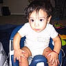Hector is registered to the contest to win money with this photo: baby, child, infant, onesie, baby_seat, blue, white, red_bracelet, toy, carpet, indoor, person, face, hair, hand, furniture, expression, sitting, clothing, home