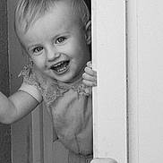 Romy a rejoint le concours — aidez-le/la à gagner de superbes lots ! toddler, child, smiling, face, door, peek, black_and_white, portrait, happy, hand, clothing, indoor, cute, young, person, baby, playful, hair, expression, standing