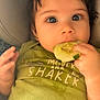 baby, child, cucumber, eating, green_shirt, car_seat, hand, face, curly_hair, cute, infant, portrait, closeup, clothing, person, healthy_food, snack, young_child, indoors, casual