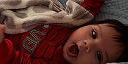 Angel is registered to the contest to win money with this photo: baby, child, blanket, bed, blue_blanket, red_clothing, onesie, lying_down, expression, mouth_open, arm_raised, soft_texture, indoor, cute, infant, face, head, sleeping_area, comfort, resting