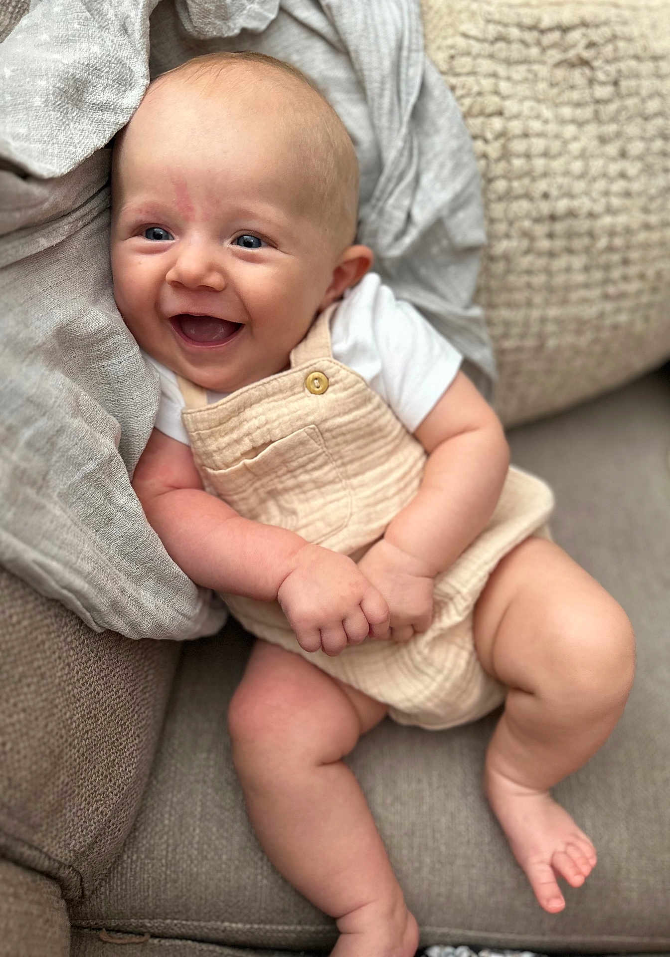 Timéo participe au concours pour gagner de l'argent avec cette photo : baby, smiling, happy, couch, blanket, infant, clothing, overalls, white_shirt, skin, face, hands, legs, foot, blue_eyes, indoor, soft_texture, comfort, cute, portrait