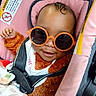 Eva is registered to the contest to win money with this photo: baby, child, sunglasses, car_seat, seatbelt, pink, orange, smile, cute, infant, clothing, blanket, face, head, sitting, portrait, indoor, happy, young, person