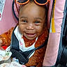 baby, smiling, car_seat, sunglasses, orange, blanket, child, happy, fuzzy_clothing, seatbelt, portrait, infant, cozy, headwear, cute, indoor, safety, baby_clothes, closeup, person