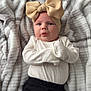 baby, infant, blanket, headband, bow, clothing, white_shirt, black_pants, lying_down, indoors, cute, expression, face, skin, person, soft_texture, pattern, cozy, portrait, young_child