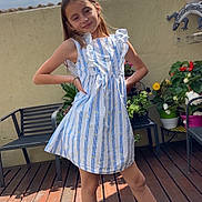 Nina a rejoint le concours — aidez-le/la à gagner de superbes lots ! child, girl, dress, striped_dress, sandals, wooden_deck, patio, potted_plants, flowers, bench, wall, clouds, sky, smile, pose, summertime, portrait, outdoor, garden, sunlight