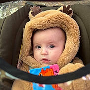Lyvia participe au concours pour gagner de l'argent avec cette photo : baby, infant, hood, hooded_jacket, car_seat, plush_fabric, blanket, soft_toy, toy_book, colorful, face, eyes, cheeks, portrait, closeup, cozy, warm_clothing, seat_harness, stroller_canopy, expression_curious