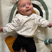 Lyana a rejoint le concours — aidez-le/la à gagner de superbes lots ! baby, black_pants, blanket, cozy, eyes, face, happy, head, heart_pattern, indoor, infant, lying_down, newborn, onesie, play_mat, portrait, smiling, socks, stacking_toy, toy