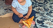 Elias joined the competition — help win amazing prizes! blue_pants, carpet, child, clothing, curious, food, foot, gray_shirt, indoor, living_room, messy_face, person, pizza, pizza_box, plush_toy, rug, sitting, snack, sofa, toddler