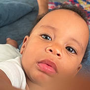 Janelle is registered to the contest to win money with this photo: baby, face, child, indoor, couch, furniture, cabinet, rug, curious, portrait, skin, eyes, mouth, hand, person, white_clothing, blur, closeup, living_room, relaxing