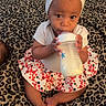 baby, bottle, milk, towel, bow, skirt, white_top, leopard_print, blanket, sitting, child, infant, cute, indoors, portrait, feet, hand, face, drinking, curious