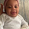 baby, carpet, child, cozy, cute, face, hand, happy, headwear, indoor, infant, person, pink_bow, portrait, sitting, skin, smiling, toddler, tongue_out, white_clothing