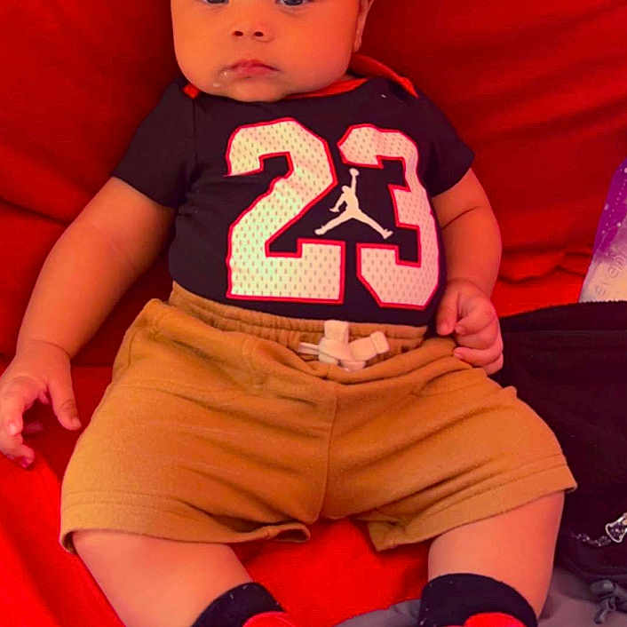 Messiah is registered to the contest to win money with this photo: baby, ball, clothing, couch, face, football, footwear, furniture, head, person, photography, portrait, shoe, shorts, sitting, sneaker, soccer, soccerball, sport, t_shirt