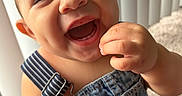 Ezrah joined the competition — help win amazing prizes! baby, smiling, happy, denim_overalls, child, portrait, indoor, cute, toddler, clothing, face, hand, skin, person, infant, closeup, joy, natural_light, striped_straps, carpet