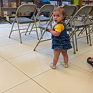 Skylar joined the competition — help win amazing prizes! bookshelf, casual_clothing, child, colorful_walls, curious, denim_dress, folding_chairs, happy, indoor, library, person, pigtails, playful, reading_area, short_hair, standing, tile_floor, toddler, window, yellow_shirt