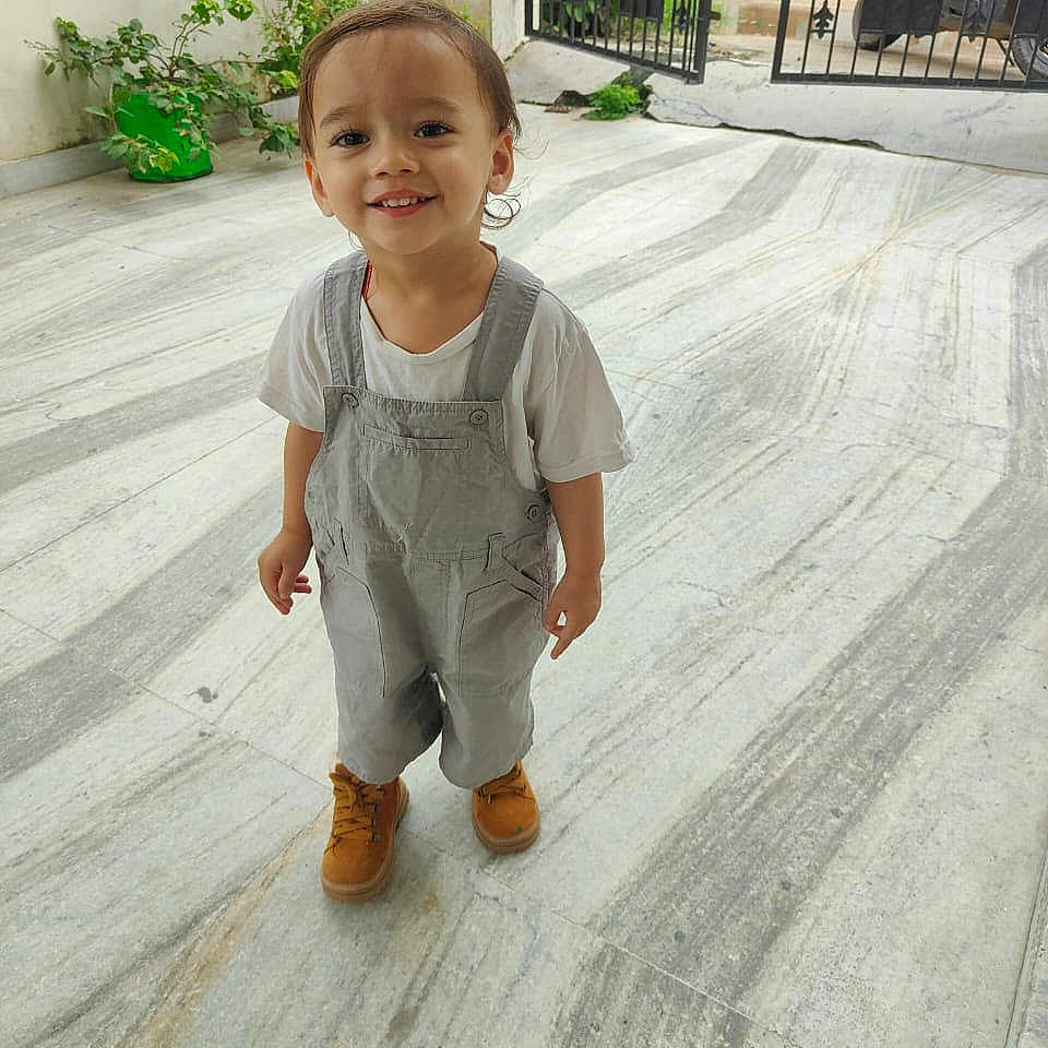 Varsashua participe au concours pour gagner de l'argent avec cette photo : boots, casual_clothing, child, cute, daylight, gate, greenery, happy, marble_floor, outdoor, overalls, person, playful, portrait, short_hair, small_person, smiling, standing, toddler, young_child