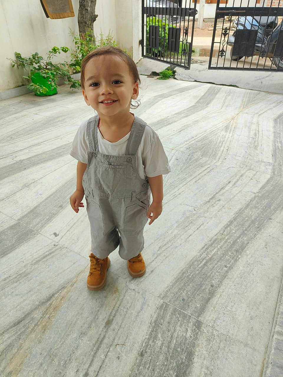 Varsashua participe au concours pour gagner de l'argent avec cette photo : toddler, child, smiling, overalls, boots, marble_floor, outdoor, gate, greenery, happy, person, young_child, casual_clothing, short_hair, standing, daylight, playful, cute, portrait, small_person