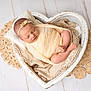 newborn, baby, sleeping, wrapped, knit_blanket, heart_shaped_bowl, crocheted_mat, soft_texture, peaceful, infant, headband, pillow, wooden_floor, cozy, portrait, cute, resting, small_feet, delicate, studio_photography