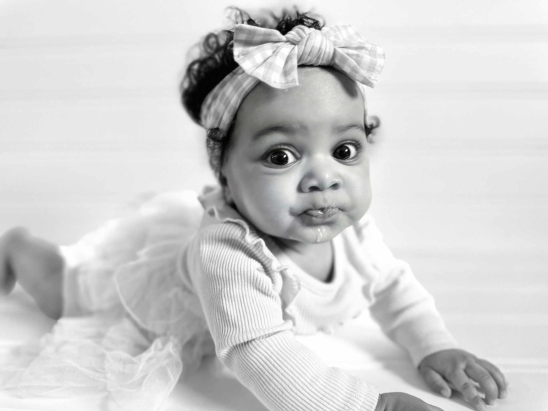 Kamiyah is registered to the contest to win money with this photo: baby, child, infant, headband, bow, crawling, curly_hair, black_and_white, portrait, closeup, cute, expression, face, hands, long_sleeve, tulle_skirt, floor, indoor, soft_light, curious