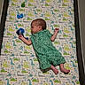 baby, newborn, infant, child, lying_down, changing_mat, dinosaur_pattern, green_outfit, onesie, toy, blue_toy, portrait, side_profile, indoor, nursery, baby_gear, sleeping_area, feet, playful, family_photo