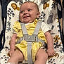 baby, infant, child, yellow_outfit, baby_seat, safety_harness, smiling, tongue_out, animal_pattern, lion, elephant, flower_pattern, indoor, cute, happy, person, small_hands, small_feet, lace_socks, playful