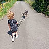 Kinay a rejoint le concours — aidez-le/la à gagner de superbes lots ! casual_clothing, child, dog, fence, greenery, leash, nature, outdoor, path, pavement, pet, road_sign, shadow, shoes, shorts, summer, sunny, toddler, trees, walking