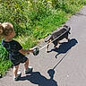 Kinay a rejoint le concours — aidez-le/la à gagner de superbes lots ! black_dog, casual_clothing, child, curly_hair, dog, grass, greenery, leash, nature, outdoor, path, plants, shadow, shorts, sidewalk, sneakers, sunlight, toddler, tshirt, walking