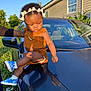 Milani is registered to the contest to win money with this photo: toddler, child, car, outdoor, sunlight, headband, bow, brown_clothing, blue_sneakers, person, hand, house, greenery, daytime, reflection, portrait, casual, support, cute, young