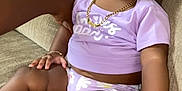 Milani is registered to the contest to win money with this photo: baby, child, purple_bows, purple_outfit, couch, sitting, cute, bracelet, necklace, white_sandals, indoor, person, infant, hand, skin, portrait, clothing, furniture, expression, young