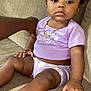baby, child, purple_bows, purple_outfit, couch, sitting, cute, bracelet, necklace, white_sandals, indoor, person, infant, hand, skin, portrait, clothing, furniture, expression, young