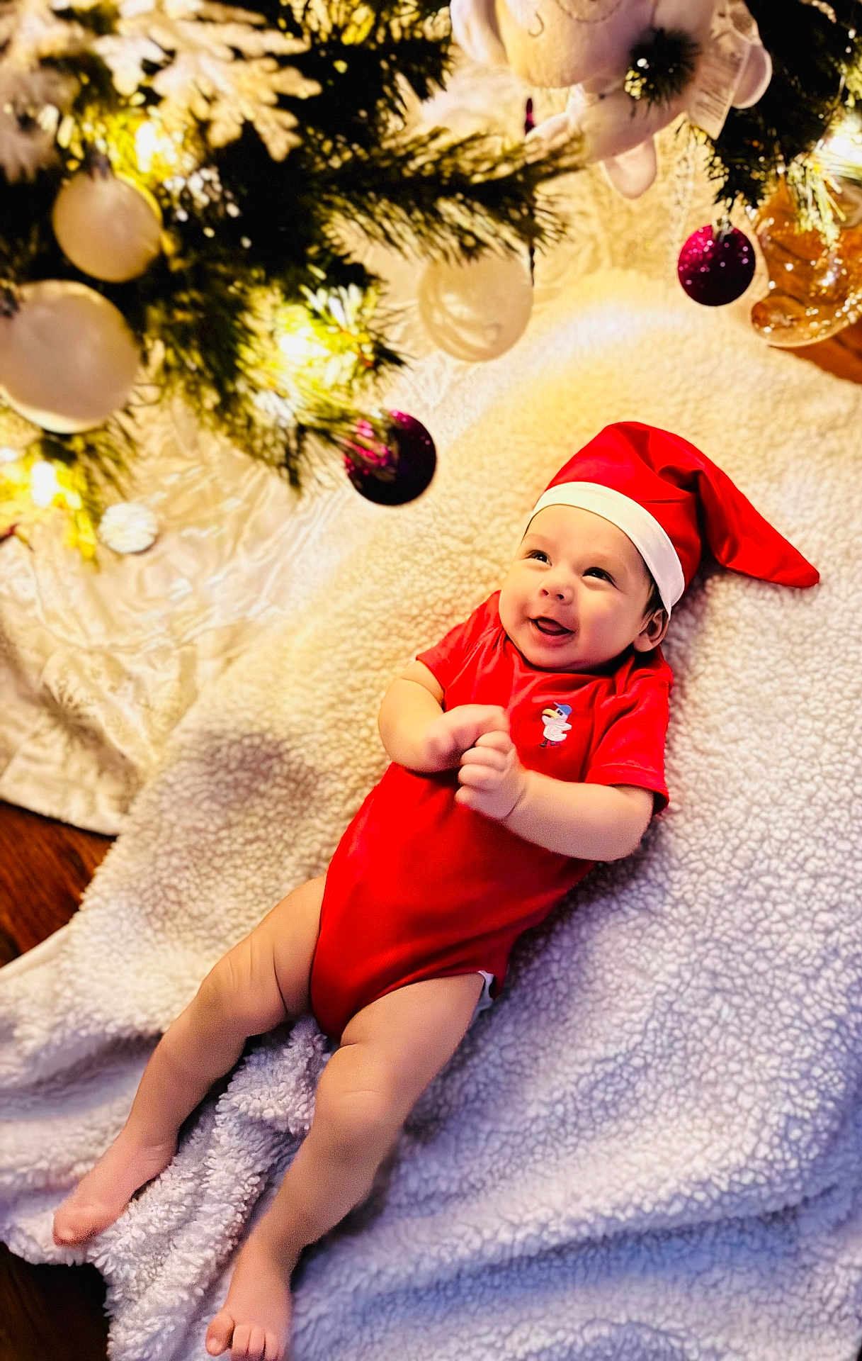 Avery joined the competition — help win amazing prizes! baby, infant, christmas, holiday, red_clothing, santa_hat, smile, blanket, tree, ornaments, lights, festive, indoors, cute, happy, lying_down, celebration, decoration, seasonal, person