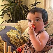 Kendra joined the competition — help win amazing prizes! baby, child, indoor, sofa, pillow, toy, red_toy, curly_hair, cute, patterned_clothing, hand, face, eyes, chewing, play, furniture, couch, living_room, small_hands, earrings