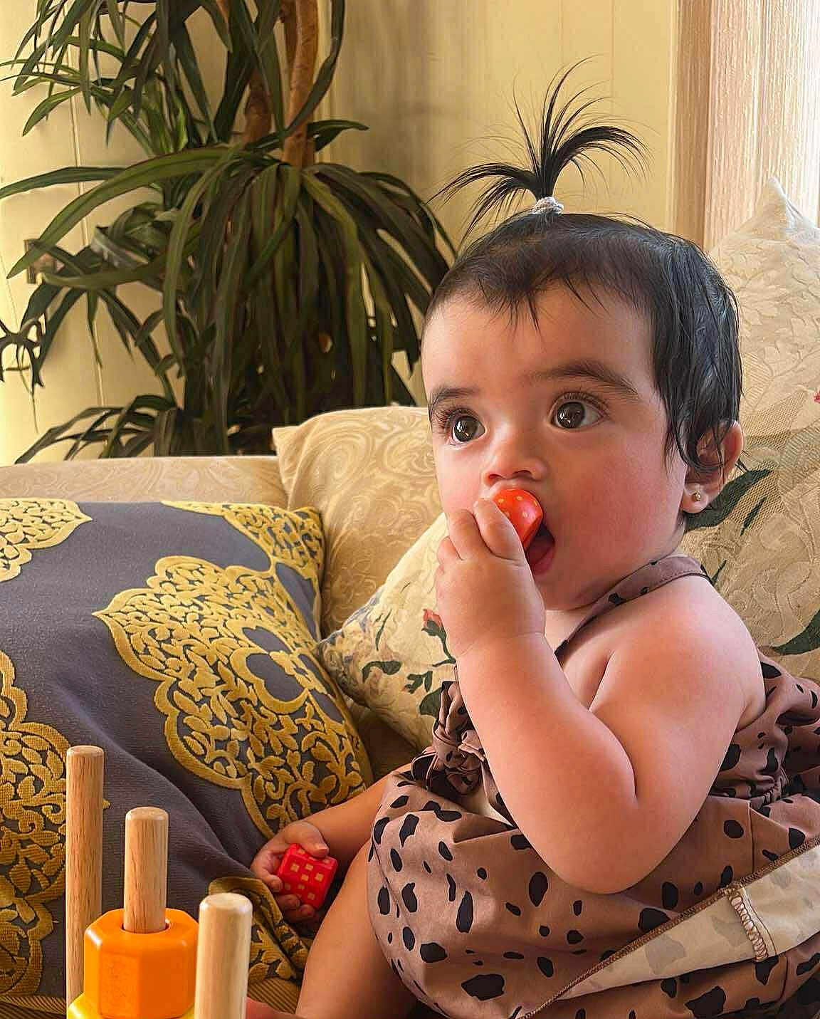 Kendra joined the competition — help win amazing prizes! baby, child, indoor, sofa, pillow, toy, red_toy, curly_hair, cute, patterned_clothing, hand, face, eyes, chewing, play, furniture, couch, living_room, small_hands, earrings