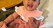 Kamryn is registered to the contest to win money with this photo: baby, child, smiling, pink_clothing, headband, baby_seat, plush_toy, mickey_mouse, happy, indoors, table, wooden_table, blanket, cushion, person, cute, infant, clothing, toddler, playful