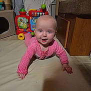 Lola joined the competition — help win amazing prizes! baby, infant, crawling, pink_onesie, toy, indoor, floor_mat, happy, child, smiling, face, head, hand, wooden_furniture, colorful, playtime, cute, home, floor, expression