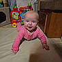 baby, infant, crawling, pink_onesie, toy, indoor, floor_mat, happy, child, smiling, face, head, hand, wooden_furniture, colorful, playtime, cute, home, floor, expression