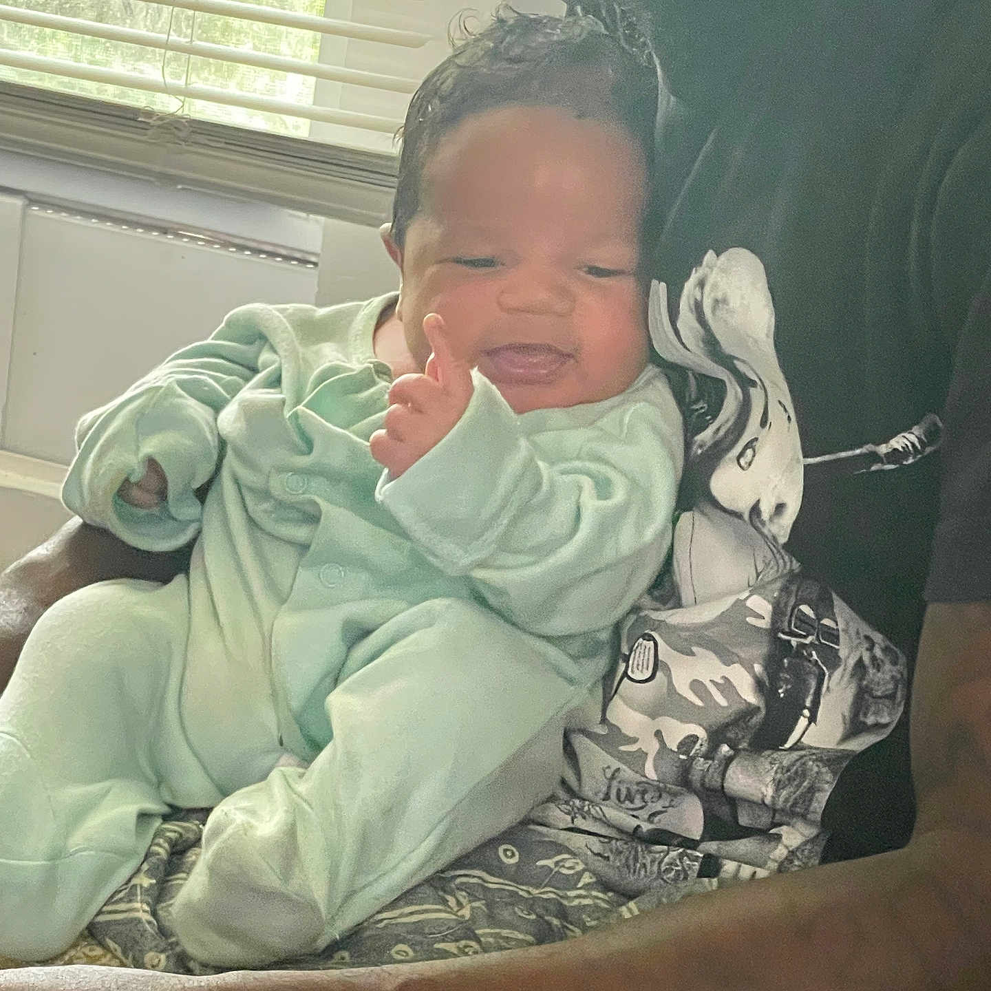 Josiah is registered to the contest to win money with this photo: baby, infant, person, adult, holding, smiling, pajamas, clothing, indoor, window, blinds, light, skin, face, arm, hand, portrait, family, cuddle, comfort