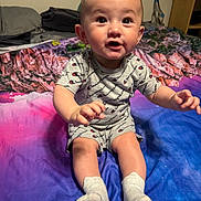 Noel joined the competition — help win amazing prizes! baby, child, infant, sitting, bed, blanket, clothing, socks, portrait, cute, indoors, expression, person, smiling, champion, colorful, young, face, hands, legs