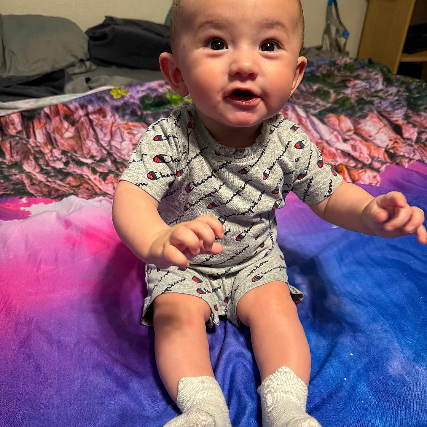 Noel joined the competition — help win amazing prizes! baby, bed, blanket, champion, child, clothing, colorful, cute, expression, face, hands, indoors, infant, legs, person, portrait, sitting, smiling, socks, young