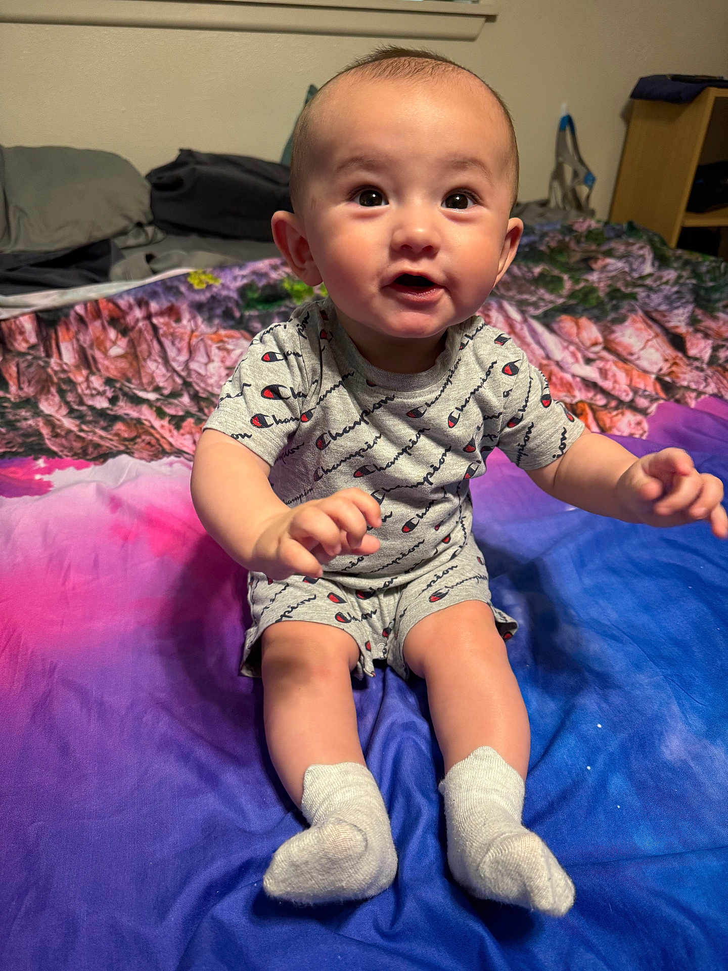 Noel joined the competition — help win amazing prizes! baby, child, infant, sitting, bed, blanket, clothing, socks, portrait, cute, indoors, expression, person, smiling, champion, colorful, young, face, hands, legs