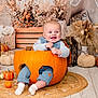 Jesse is registered to the contest to win money with this photo: baby, pumpkin, smile, autumn, fall, lantern, dried_flowers, decor, orange, blue_clothing, carved_pumpkin, floor, rug, happy, cute, indoor, festive, seasonal, child, cozy