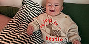 Jesse joined the competition — help win amazing prizes! baby, child, smiling, sweatshirt, reindeer, pillow, striped_pillow, green_pillow, bed, cozy, happy, cute, socks, fuzzy_socks, pants, infant, indoors, person, seated, clothing