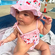 Wrenlee joined the competition — help win amazing prizes! baby, child, swimsuit, hat, pink, cherry_pattern, towel, poolside, hand, outdoor, summer, sunhat, person, skin, legs, arm, table, chair, cone, daylight