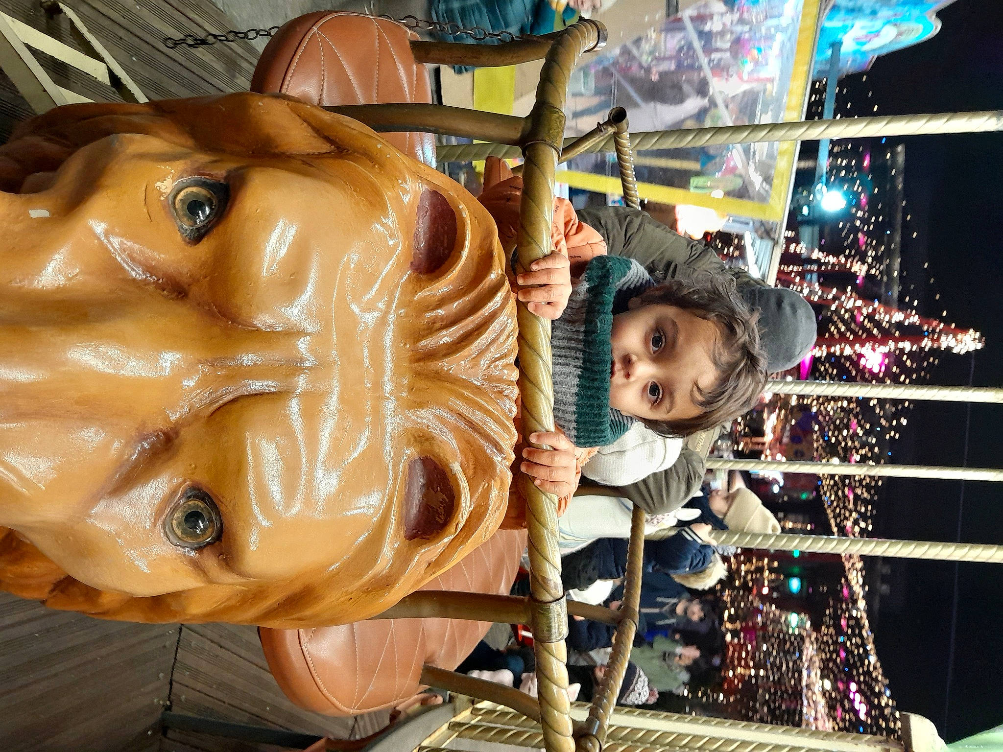 Lilian participe au concours pour gagner de l'argent avec cette photo : art, carousel, carving, chainsaw_carving, child, city, event, fawn, fun, hat, headwear, leisure, metal, person, personal_protective_equipment, public_event, recreation, sculpture, statue, toddler