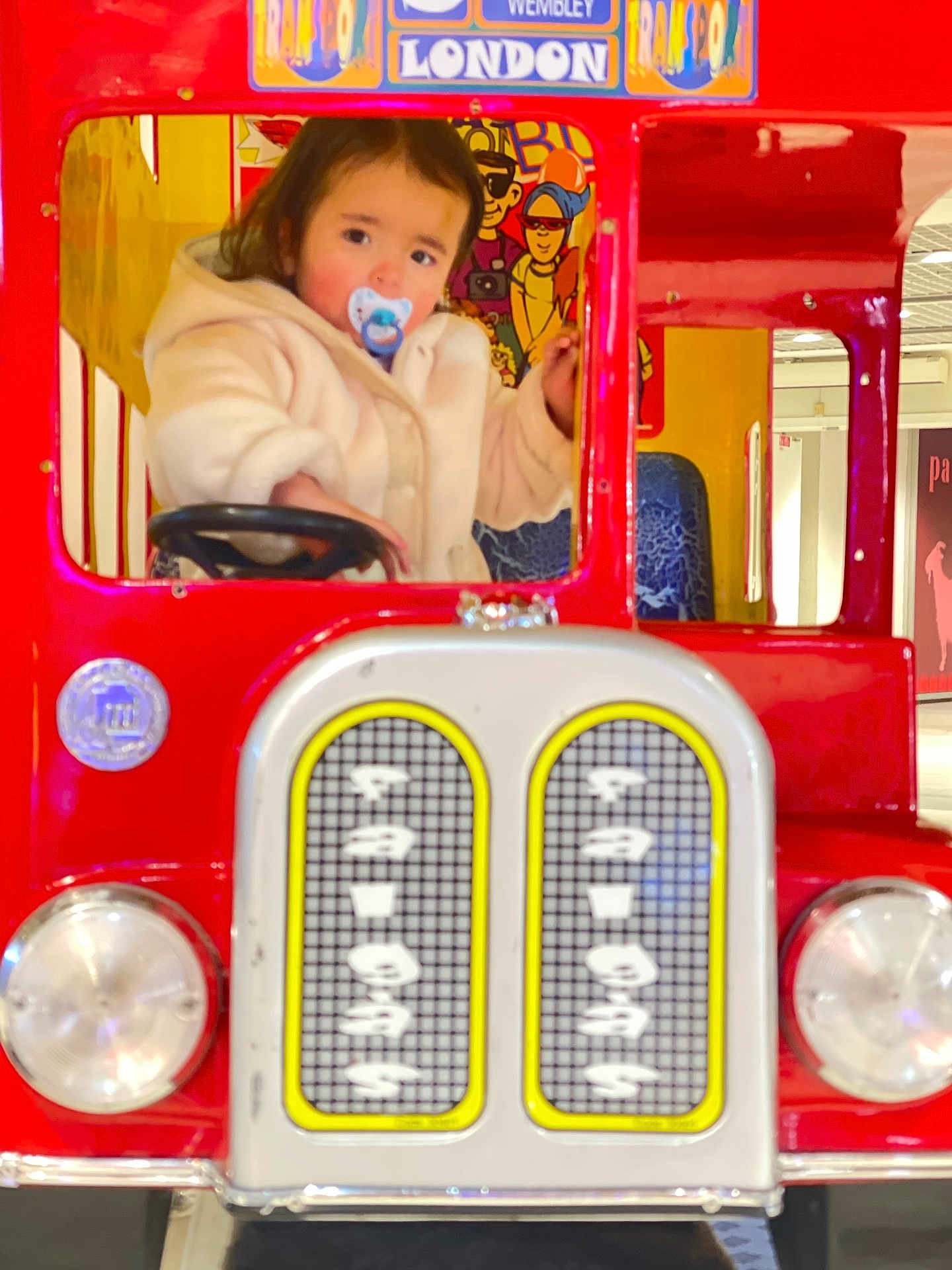 Harvy a rejoint le concours — aidez-le/la à gagner de superbes lots ! toddler, child, pacifier, toy_bus, red, beige_jacket, indoor, steering_wheel, play_area, colorful, face, portrait, cute, window, cartoon, seat, person, playground, clothing, young_child