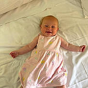 Isla joined the competition — help win amazing prizes! arms_outstretched, baby, bed, child, comfort, cute, dress, floral, happy, indoors, infant, legs_spread, lying_down, person, pillow, pink, portrait, smiling, soft_lighting, white_bed