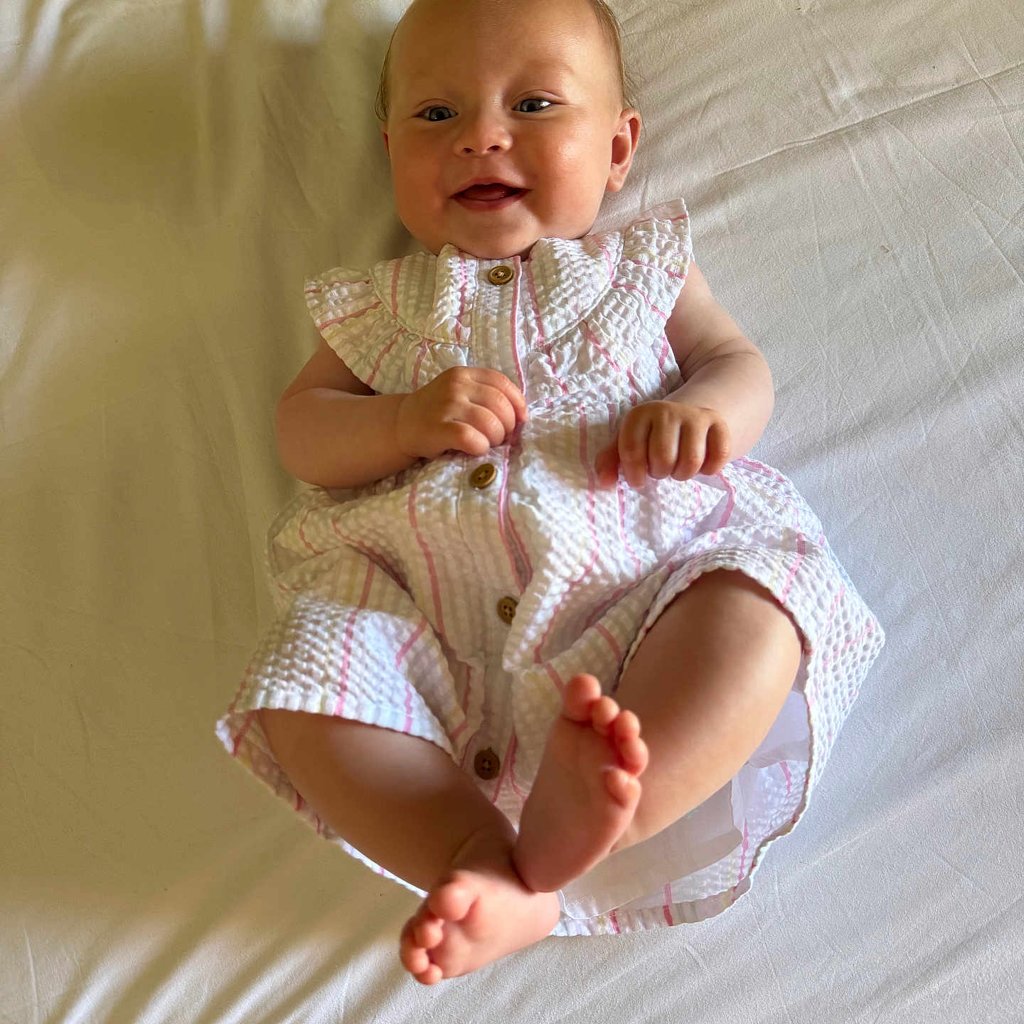 Isla joined the competition — help win amazing prizes! baby, buttoned_dress, child, cute, dress, feet, hands, happy, indoors, infant, lying_down, person, playful, portrait, skin, sleepwear, smiling, soft_light, white_bed, young_child