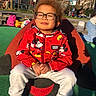 Noha participe au concours pour gagner de l'argent avec cette photo : backpack, casual_clothing, child, daytime, glasses, happy, mickey_mouse, outdoor, park, people, person, play_equipment, playground, red_jacket, seated, smile, sneakers, sunlight, trees, white_pants