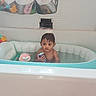 Obed is registered to the contest to win money with this photo: baby, bare_shoulders, bath_toy, bathroom, bathtub, child, dark_hair, facial_expression, home, indoor, pink_toy, plush_toy, portrait, sitting, tile_wall, toddler, toy, turquoise, water, wet