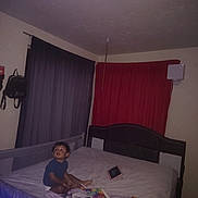 Obed is registered to the contest to win money with this photo: bed, bedroom, blanket, blue_shirt, child, colorful_blanket, curtains, flash_photography, furniture, home, indoor, looking_up, nighttime, portrait, purple, red, short_hair, sitting, tablet, toddler
