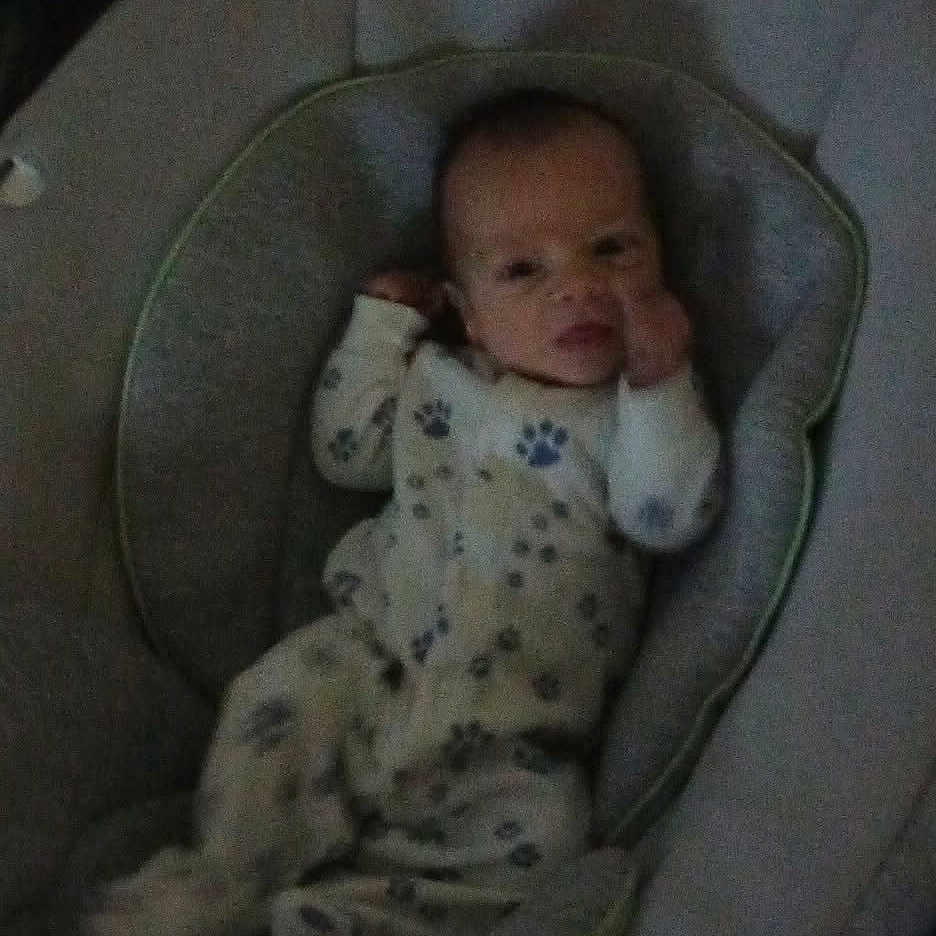 Dalton is registered to the contest to win money with this photo: baby, baby_bouncer, child, cozy, cushion, face, head, indoors, infant, looking_at_camera, lying_down, nursery_item, onesie, pajamas, paw_prints, portrait, seat, sleepwear, small_person, soft_furniture